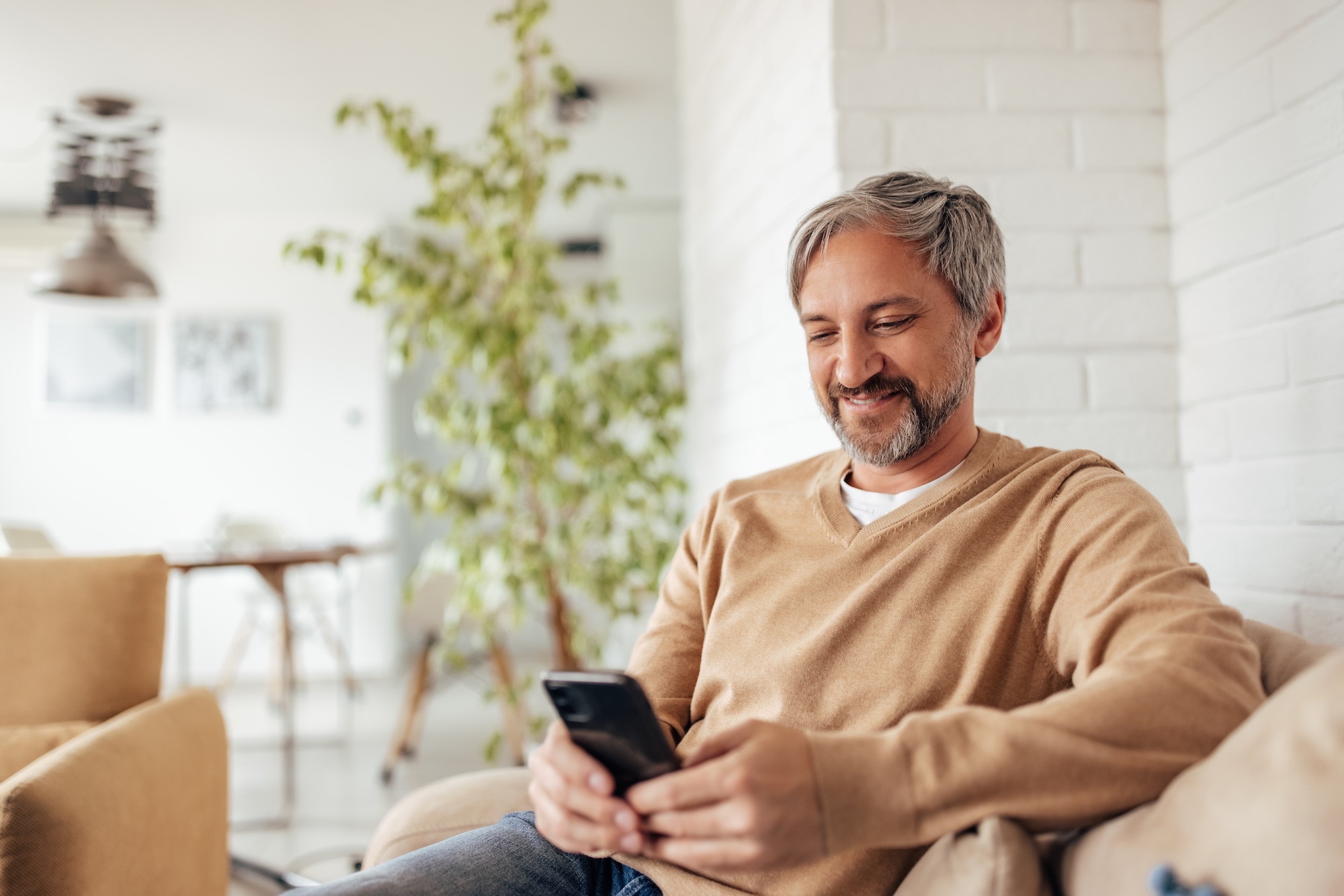An older man sitting on his couch at home smiling after booking at appointment with Crescent Beach Care for non-surgical fat loss in St. Augustine.